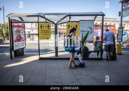 I negozi non essenziali iniziano ad aprirsi in tutto il Regno Unito mentre la distanza sociale continua. Una donna si trova a una fermata dell'autobus con la sua fabbrica di famiglia acquistata presso una fermata dell'autobus nel sud-ovest di Londra il primo giorno in cui i negozi non essenziali sono stati abilitati ad aprire. 01 Giugno 2020. Wimbledon, Southwest London, UK Credit: Jeff Gilbert/Alamy Live News Foto Stock