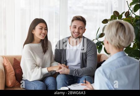 Sorridenti coniugi multietnici mani che riconciliano i loro collaboratori seduti nell'Ufficio Psicoterapeuta Foto Stock