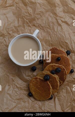 Caffè e pancake serviti con mirtilli sulla carta stropicciata. Spazio negativo. Composizione verticale. Foto Stock