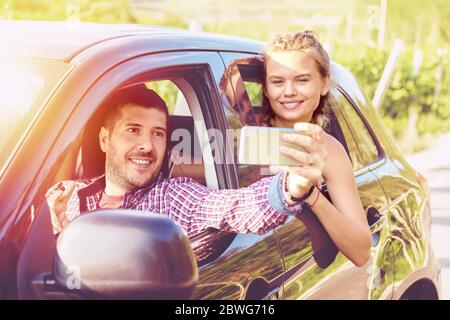 Felici coppie giovani in viaggio su strada prendendo selfie mentre si guida su strada di campagna Foto Stock