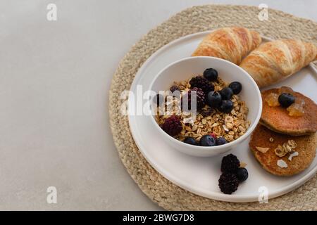 Piatto per la colazione sano e nutriente con muesli, frittelle di farinata d'avena e croissant. Composizione orizzontale. Spazio negativo. Foto Stock