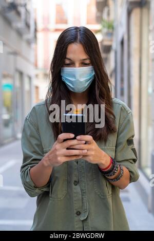 Donna che indossa una maschera protettiva sul viso mentre usa il telefono cellulare per strada Foto Stock