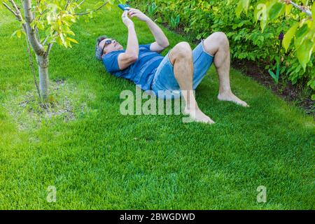 Vista di uomo che si posa su prato verde erba vicino alla mela e controllare il suo cellulare. Foto Stock