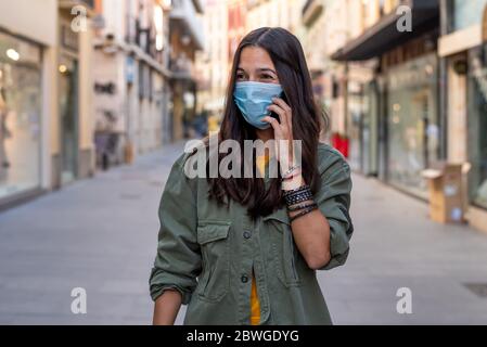 Donna che indossa una maschera protettiva sul viso mentre usa il telefono cellulare per strada Foto Stock