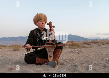 Musicista kirghiso che suona uno strumento musicale tradizionale conosciuto come Komuz, a Issyk Kul, Kirghizistan Foto Stock