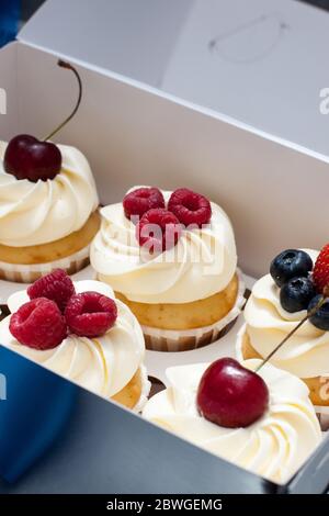 Cupcake con panna montata, ciliegie fresche, lamponi, mirtilli, fragole in scatola regalo con nastro blu. Foto Stock