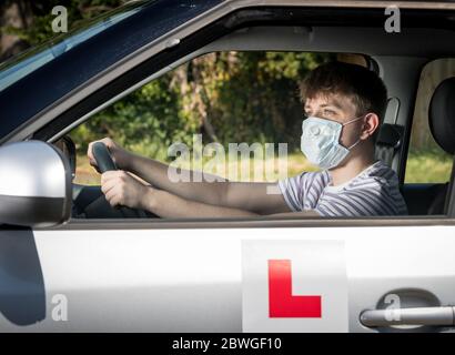 Teenage allievo driver un indossare una maschera a causa della pandemia del coronavirus in attesa di iniziare la sua lezione di guida. Foto Stock