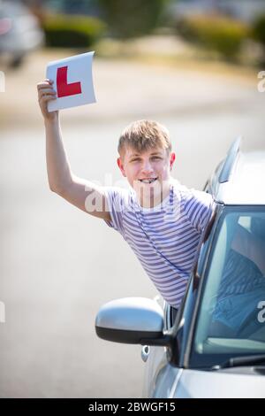 L'allievo teenager driver festeggia il superamento del test di guida sventolando i suoi piatti a L in aria. Foto Stock