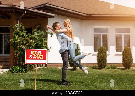 Bella giovane coppia abbracciando di fronte alla loro nuova casa, all'aperto Foto Stock