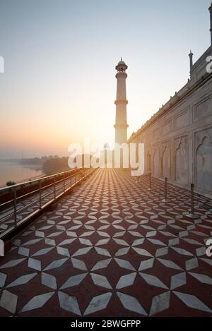 Una sezione del Taj Mahal che corre lungo il fiume Yamuna, con il sole che sorge dietro un minareto Foto Stock