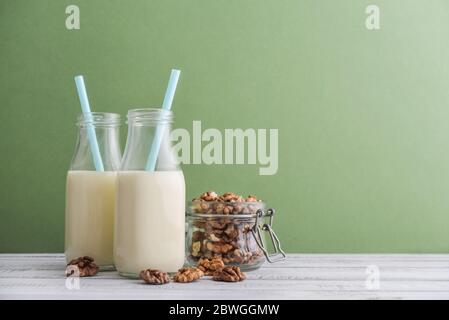 Due bottiglie di latte di noce vegetariano con noce in vaso su sfondo blu Foto Stock