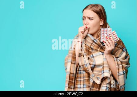 Donna con infezione tiene le pillole nelle sue mani avvolte in un plaid. Sfondo blu Foto Stock