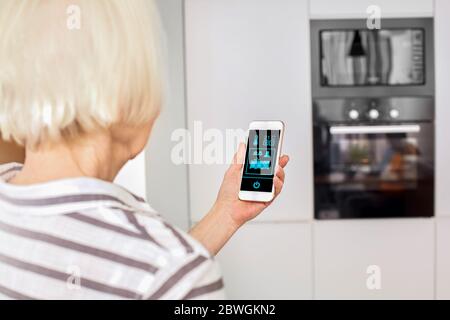 Pensione. Donna anziana che controlla la casa intelligente sullo smartphone vista posteriore primo piano controllo della temperatura Foto Stock