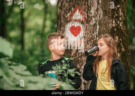 Ragazzo piccolo che chiacchiera con la ragazza carina nella foresta, trascorrendo del tempo nella natura primaverile. I bambini bevono il tè da thermos mentre si rompono nella foresta. Foto Stock