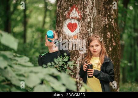 Ragazzo piccolo che chiacchiera con la ragazza carina nella foresta, trascorrendo del tempo nella natura primaverile. I bambini bevono il tè da thermos mentre si rompono nella foresta. Foto Stock