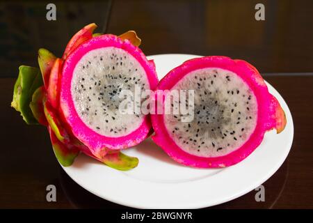 Due fette di Pitaya su un piatto bianco e tavolo scuro Foto Stock