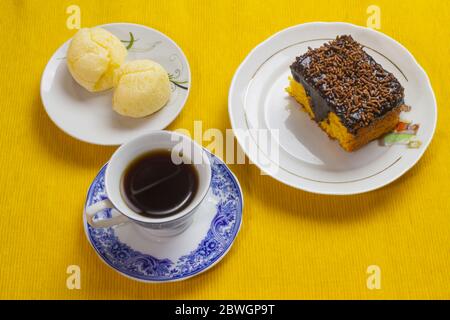 Torta di carote cioccolato a base di glassa, pane al formaggio brasiliano e tazza di caffè e sul placemat giallo. Foto Stock