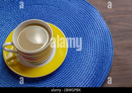 Caffè con latte in tazza colorata su placemat blu e tavolo di legno. Foto Stock