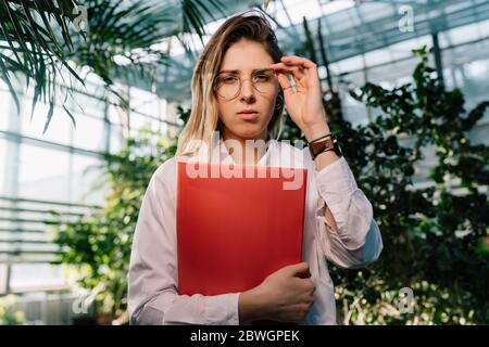 Giovane ingegnere agricolo che lavora in serra. Giovane scienziata femminile che guarda la macchina fotografica Foto Stock