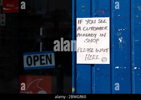 Piccolo negozio durante la pandemia di coronavirus - firmare all'esterno limitando i clienti a uno alla volta, Shawlands, Glasgow, Scozia, Regno Unito Foto Stock