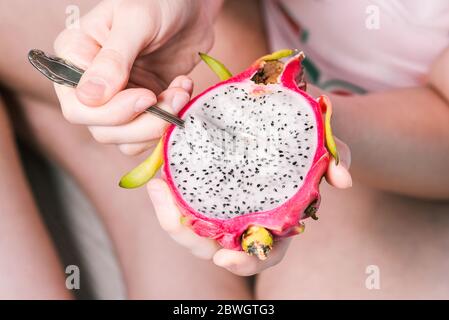 Una ragazza mangia la polpa di un frutto di drago esotico dalla Thailandia con un cucchiaio. Primo piano su Fresh pitaya. Cibo vegano e sano Foto Stock