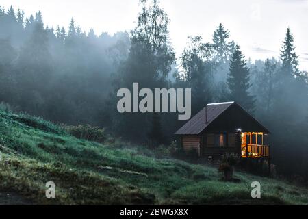 Piccola vecchia casa di legno in foresta di nebbia. Paesaggi di montagna. Immagine concettuale della natura Foto Stock