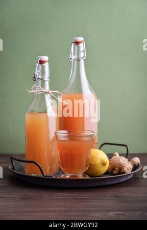 Tè Kombucha crudo fermentato in casa in vetro e bottiglia con limone e zenzero su sfondo verde Foto Stock