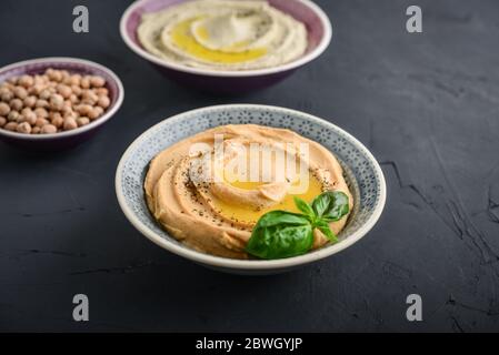 Ciotole con diversi tipi di hummus su sfondo nero, primo piano Foto Stock