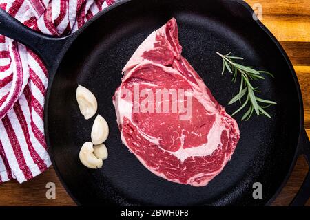Una fotografia di una bistecca di ribeye disossata con aglio e rosmarino in una padella di ghisa che si prepara per essere cucinata Foto Stock