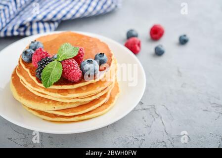 Pancake con frutti di bosco freschi e sciroppo d'acero sul piatto su fondo grigio Foto Stock