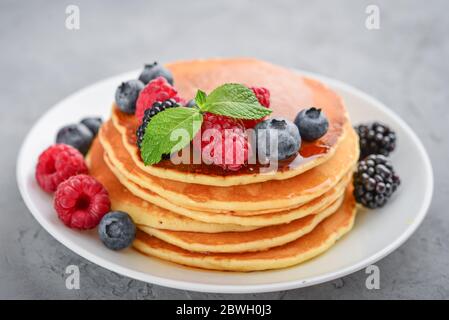 Pancake con frutti di bosco freschi e sciroppo d'acero sul piatto su fondo grigio Foto Stock
