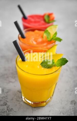 Frullati freschi di fragola, mango e papaia in bicchieri su sfondo grigio. Foto Stock