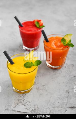 Frullati freschi di fragola, mango e papaia in bicchieri su sfondo grigio. Foto Stock