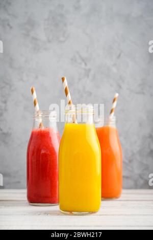 Frullati freschi di fragola, mango e papaia in bottiglie su sfondo di legno blu Foto Stock