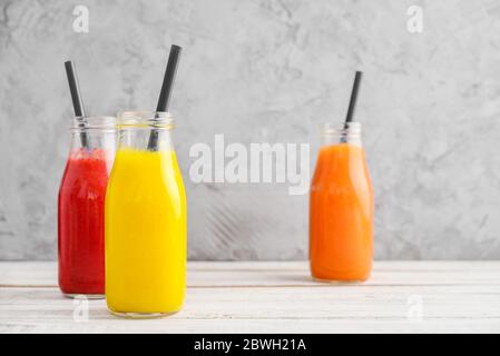 Frullati freschi di fragola, mango e papaia in bottiglie su sfondo grigio. Foto Stock