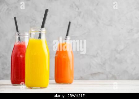 Frullati freschi di fragola, mango e papaia in bottiglie su sfondo grigio. Foto Stock