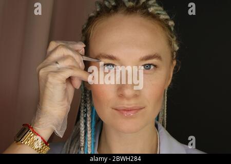 Ritratto di una bella giovane donna brow designer con un dreadlock blu e bianco e pinzette in mano closeup Foto Stock