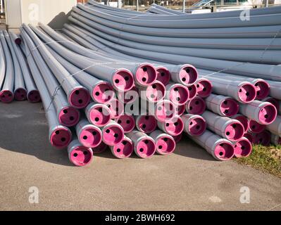 Nuovi tubi di fognatura grigi, impacchettati con cavi in plastica grigia con coperchi color magenta, sono pronti per essere posati accanto alla strada. Foto Stock