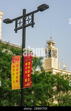 Xian, Cina - 30 aprile 2010: Vista del centro. Torre dell'orologio bianca e striscioni gialli e rossi contro il cielo blu con fogliame verde. Foto Stock