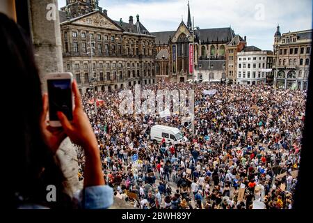 Una donna, registra un video con il suo telefono della folla di protesta riunita a piazza Dam attraverso un edificio di finestre. Migliaia di persone prendono parte alla protesta 'Black Lives Matter' tenutasi a Piazza Dam ad Amsterdam, per protestare contro la recente uccisione di George Floyd, Un uomo nero morto in custodia di polizia a Minneapolis, negli Stati Uniti, dopo essere stato trattenuto dagli agenti di polizia di Minneapolis il giorno del Memorial Day. Foto Stock