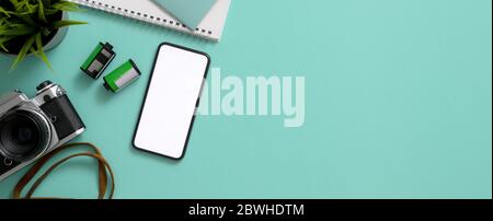 Vista dall'alto del piano di lavoro creativo con smartphone, fotocamera, notebook, pentola ad albero e spazio per la copia su un tavolo turchese Foto Stock