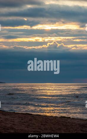 L'oceano si rigondisca con onde infrangenti. Luce del sole che splende attraverso le aperture nelle nubi. Brillantini che si riflettono sulle acque. Cavendish Beach, PEI, Canada. Foto Stock