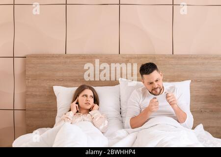 La giovane donna non può dormire a causa del marito che gioca a giocare sul telefono cellulare in camera da letto Foto Stock