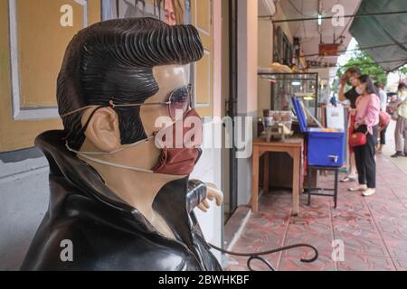 Durante la pandemia di Covid-19 (nCorona) nel 2020, una statua seduta di Elvis Presley di fronte ad un caffè a Bangkok, Thailandia, indossa una maschera facciale Foto Stock