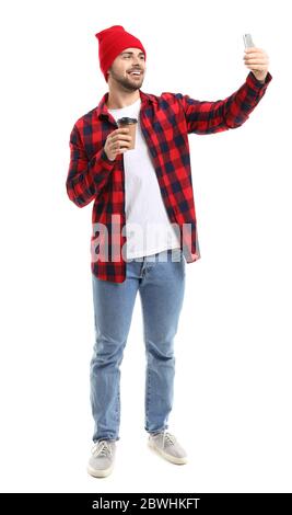 Giovane uomo con tazza di caffè caldo che prende selfie su sfondo bianco Foto Stock