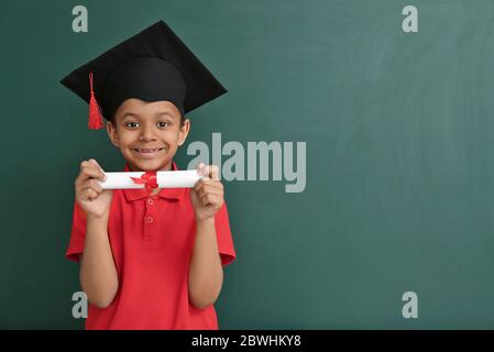 Piccolo afroamericano in cappello di laurea e con diploma vicino a lavagna Foto Stock