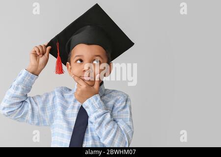 Premuroso ragazzo afroamericano in cappello di laurea su sfondo grigio Foto Stock