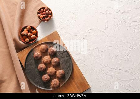 Piatto con gustose caramelle al cioccolato e nocciole su sfondo bianco Foto Stock