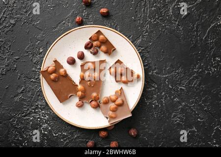 Piatto con gustoso cioccolato e nocciole su sfondo scuro Foto Stock