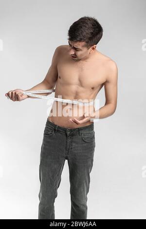 Uomo malato che misura la vita su sfondo colorato. Concetto di anoressia Foto Stock